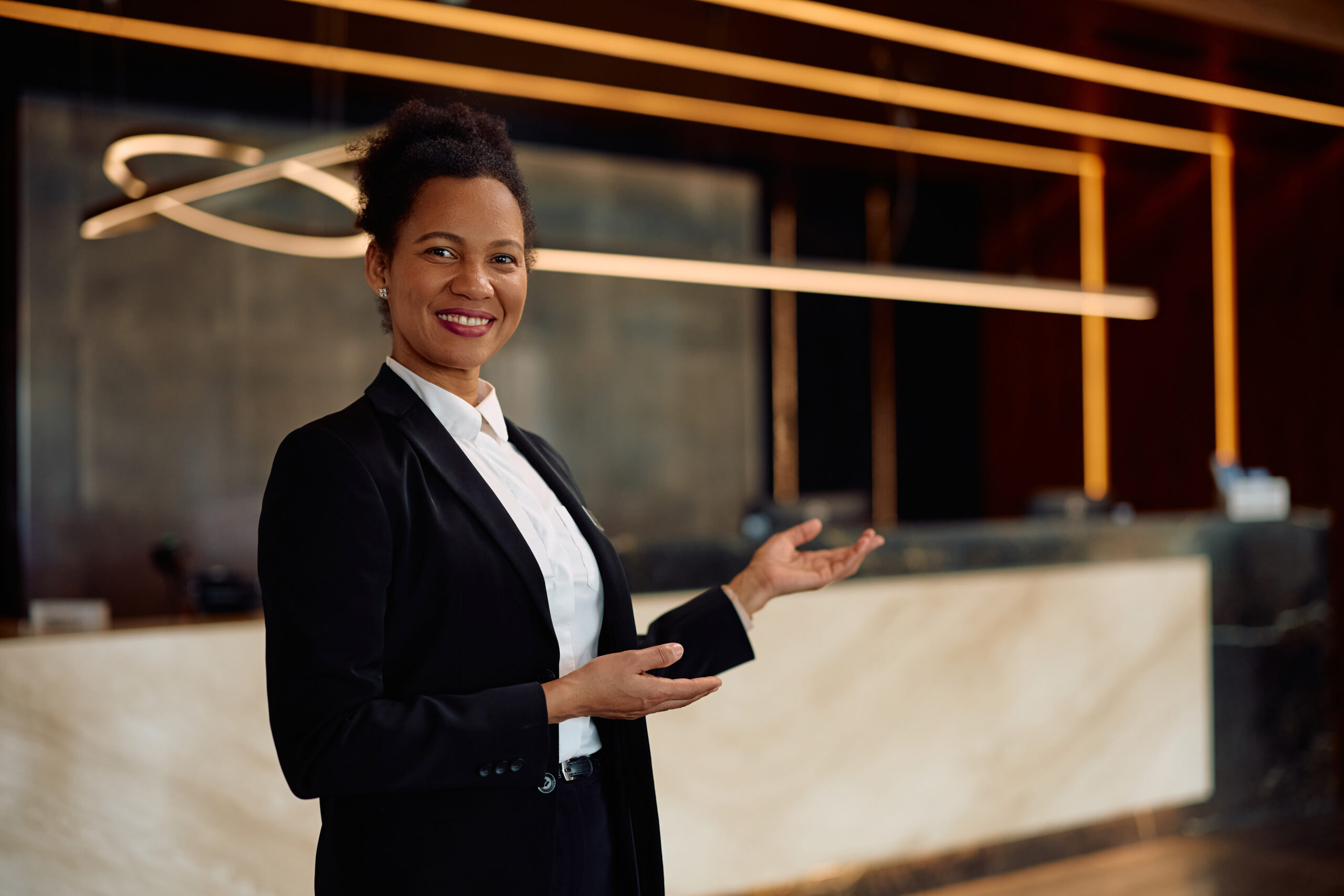 Happy black concierge welcoming guests in a hotel and looking at camera.
